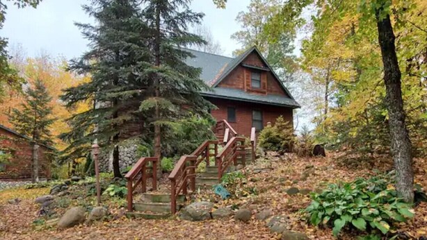 A cabin with a stone staircase leading to a wooden deck surrounded by trees and autumn leaves.