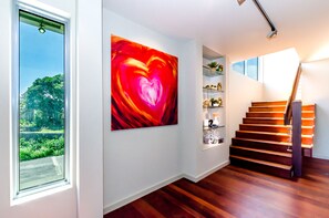 A modern interior with a staircase, a large abstract painting, and a view through a window.