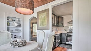 A dining area with a round table, white chairs, and a decorative centerpiece. There is a kitchen visible in the background with modern appliances and cabinets. - Chincoteague Island Cottage ~ 2 Mi to Beaches (Chincoteague)