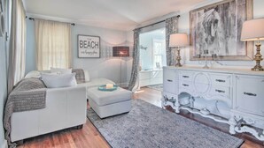 A bedroom with a bed, a white dresser, a large painting, and a wall with a 'BEACH' sign. - Chincoteague Island Cottage ~ 2 Mi to Beaches (Chincoteague)