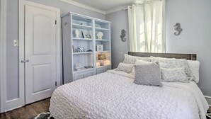 A bedroom with a large bed, a white wardrobe, a built-in shelving unit, and decorative wall art. - Chincoteague Island Cottage ~ 2 Mi to Beaches (Chincoteague)