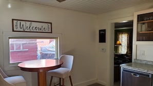 A small kitchen with a round wooden table, two white chairs, a ceiling fan, and a window with a view of a red brick building. - Best in the Bay!! 3B/1.5ba, Pet friendly Home (Alexandria Bay)