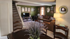 A living room with a staircase, a television, a fireplace, and a dining area with a table and chairs. - Best in the Bay!! 3B/1.5ba, Pet friendly Home (Alexandria Bay)