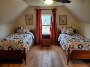 Ein Schlafzimmer mit zwei Betten, Holzboden, Deckenventilator und einem Fenster mit Vorhängen.