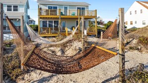 A beachfront property with a two-story house featuring a balcony and a hammock in the foreground. - Oceanfront Family Cottage: Hot Tub, Heated Pool. Game Room & Stunning Beach View (Atlantic Beach)