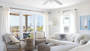 A coastal room with a white color scheme, featuring a wicker chair, a cushioned sofa, and a ceiling fan. - Oceanfront Family Cottage: Hot Tub, Heated Pool. Game Room & Stunning Beach View (Atlantic Beach)