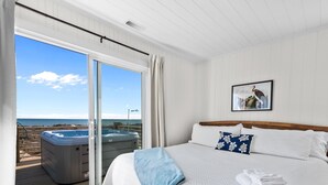 A bedroom with a large bed, a hot tub, and a view of the beach. - Oceanfront Family Cottage: Hot Tub, Heated Pool. Game Room & Stunning Beach View (Atlantic Beach)
