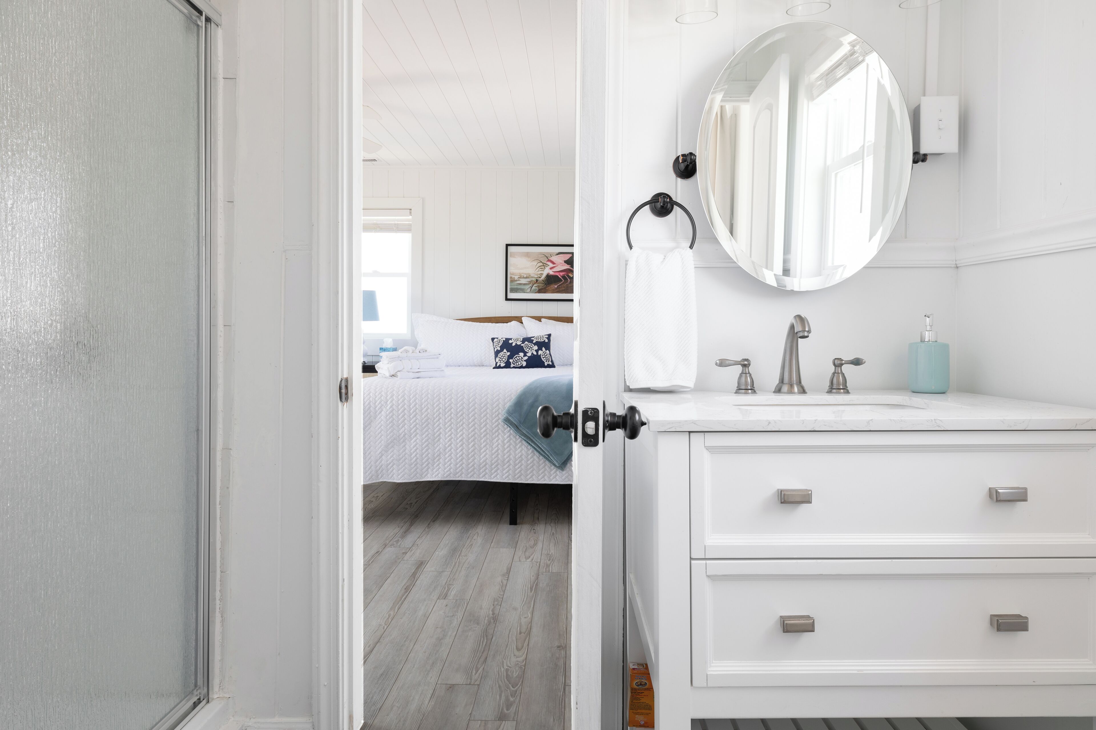 Une chambre d’hôtel avec un lit, une coiffeuse blanche avec un miroir et une salle de bain équipée d’un lavabo et de toilettes.