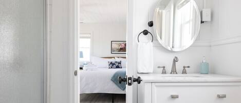 Une chambre d’hôtel avec un lit, une coiffeuse blanche avec un miroir et une salle de bain équipée d’un lavabo et de toilettes.