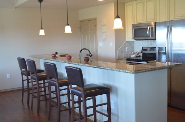 A kitchen with a central island, bar stools, stainless steel appliances, and pendant lighting.