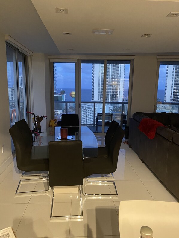 A modern living room with a glass dining table, black chairs, and a grey sofa. - Beautiful 2 bedroom condo w/ocean views (Hallandale Beach)