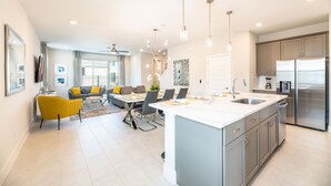 Une cuisine moderne dotée d’un îlot central, d’appareils électroménagers en acier inoxydable et de luminaires suspendus.
