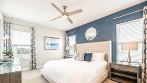 Une chambre moderne avec un grand lit, un ventilateur de plafond, un miroir rond et une table de chevet avec une lampe.