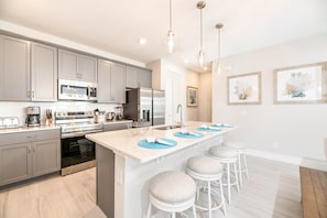 A modern kitchen with grey cabinets, stainless steel appliances, and a central island with bar stools.