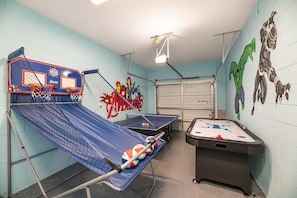 A recreational room with a basketball hoop, ping pong table, and foosball table.