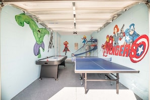 A room with a foosball table, a ping pong table, and walls decorated with superhero murals.