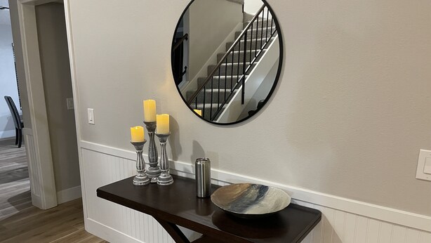 A wooden console table with a mirror, candles, and a decorative bowl against a wall with a staircase in the background. - Comfortable home with sparkling private pool minutes to the Strip! (Henderson)