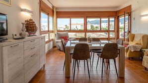 Un salón amplio con mesa de comedor, asientos cómodos, televisión y ventanas grandes con vistas al paisaje.