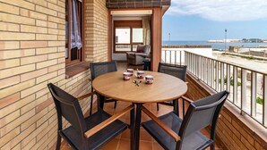 Un balcón con una mesa redonda de madera y cuatro sillas, vista al mar y un muro de ladrillo.