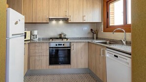Una cocina compacta con armarios de madera, horno empotrado, estufa, lavamanos y ventana.
