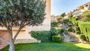 Un jardin bien entretenu, avec un arbre, des haies soigneusement taillées et un escalier en pierre menant à un bâtiment.