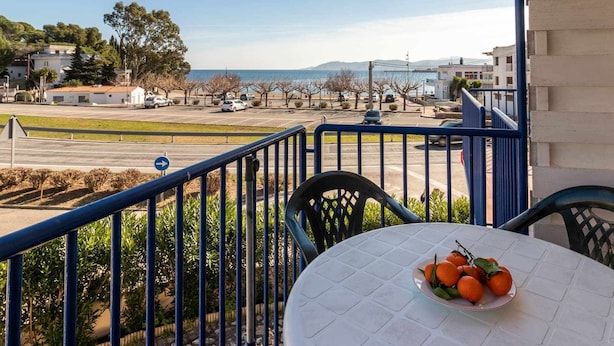 Ein Balkon mit Tisch und Stühlen, der auf einen Parkplatz und ein Gewässer blickt.