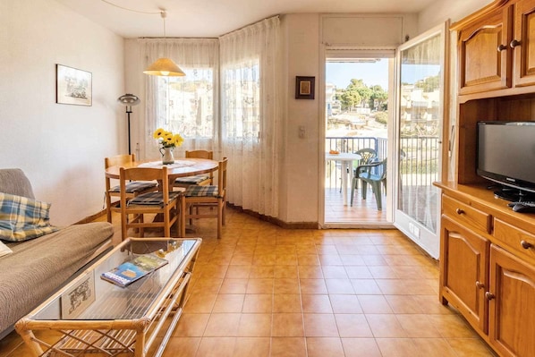A cozy living room with a sofa, coffee table, dining table with chairs, a TV, and a balcony with outdoor furniture.
