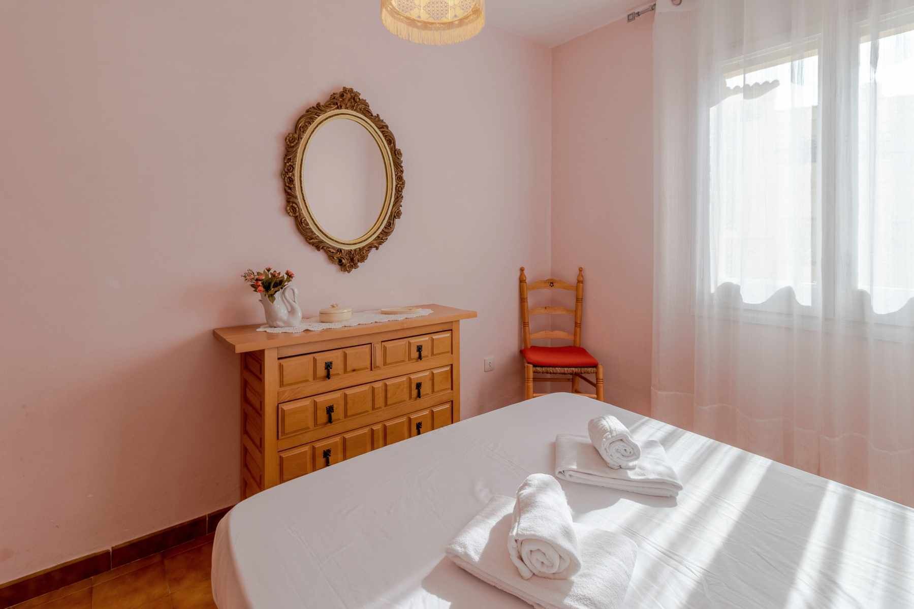 Une chambre à coucher avec un lit, une commode en bois, un miroir et une chaise.