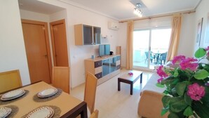 Un salon moderne comprenant un coin repas, un téléviseur et un balcon aménagé avec du mobilier d’extérieur.
