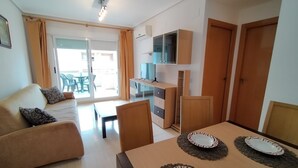 Uma sala de estar moderna com um sofá, uma mesa de jantar posta com pratos, uma televisão e uma porta de vidro deslizante que dá para uma área externa.