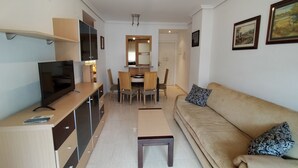 Uma sala de estar moderna com sofá, televisão e um espaço de refeições com cadeiras e mesa.