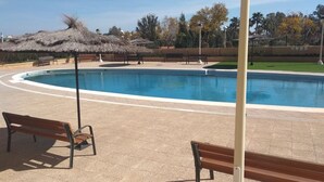 Uma piscina com cobertura de palha, rodeada por bancos e um deck pavimentado.