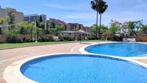 Zona de piscina con dos piscinas, rodeada de un camino de ladrillo y vegetación.