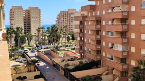 Un edificio residencial de varios pisos con balcones, un estacionamiento y palmeras.