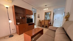 Una sala de estar con sofá, aparador de madera, televisor y un comedor con sillas y mesa.