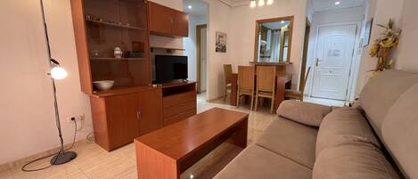 A living room with a sofa, wooden cabinet, TV, and a dining area with chairs and a table.