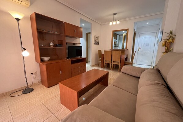 A living room with a sofa, wooden cabinet, TV, and a dining area with chairs and a table. - ACV - Costa Caribe II-2ª Línea Planta 4 Sur (Oropesa del Mar)