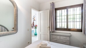 Ein Schlafzimmer mit Bett, Schminktisch, Spiegel und einem Fenster mit Vorhängen.