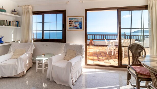 Ein heller Wohnraum mit Meerblick, ein Balkon mit Sitzgelegenheit im Freien und ein Essbereich.