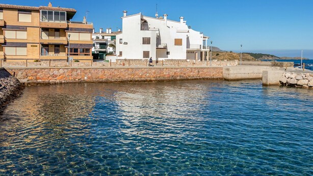 Un edificio frente al mar, con vistas despejadas, una pared de piedra y un sendero pavimentado.