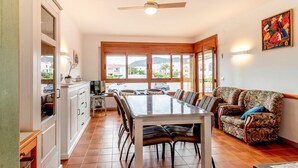 Amplia sala de estar con mesa de comedor, sofá y ventanas grandes que ofrecen vistas al exterior.