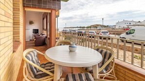Un balcón con sillas de mimbre y una mesa, con vista a un estacionamiento y la playa.