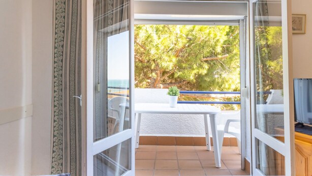 Puerta corrediza de vidrio abierta que da a un patio exterior con una mesa blanca, sillas y una pequeña planta en maceta.