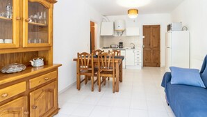 Una cocina compacta con armarios blancos, una mesa de comedor con sillas, un sofá azul y un mueble de madera con puertas de cristal.