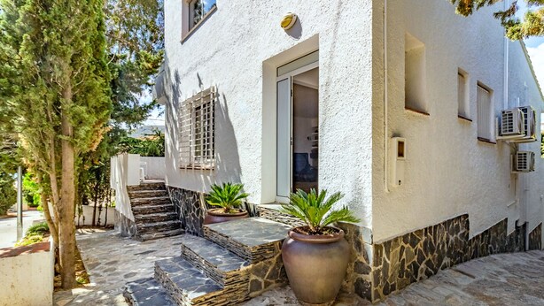A white building with a stone staircase leading to a door, potted plants, and a tree.