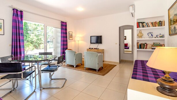 A modern living room with a dining table, two armchairs, a sofa, a TV, and a bookshelf.