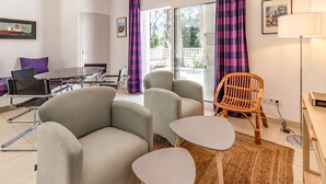 A modern living room with two grey sofas, a small white table, a wicker chair, and a dining table with chairs.