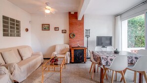 A living room with a sofa, a coffee table, a fireplace, a TV, and a dining area with chairs and a table. - Les Tonyines 68 - apartment with views and terrace (Llança)
