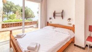 A neatly made bed with white linens and towels, a wooden headboard, and a view of greenery and a body of water through a large window. - Les Tonyines 68 - apartment with views and terrace (Llança)