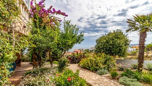 Un giardino con un sentiero in pietra, diverse piante e vista sul mare.